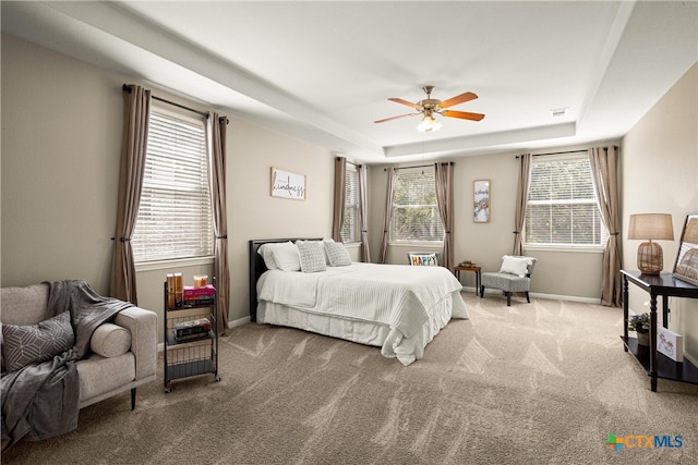 bedroom with ceiling fan, multiple windows, a tray ceiling, and light colored carpet