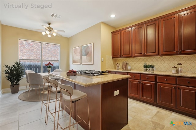 12109 Bryony Dr, Austin, TX 78739 - kitchen with a breakfast bar area, decorative backsplash, light stone counters, a center island, and gas cooktop