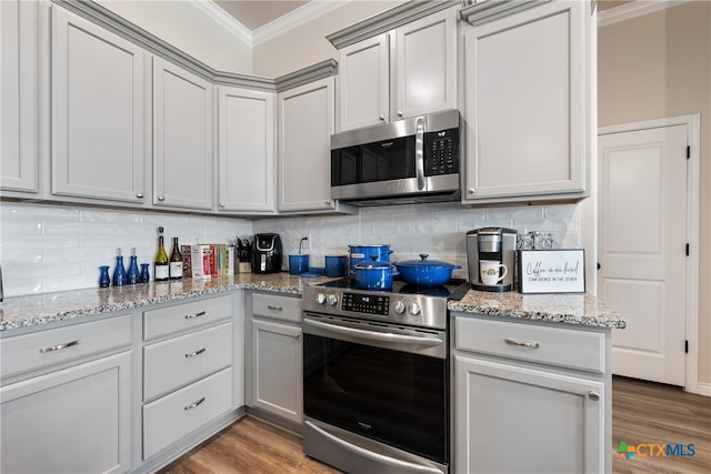 kitchen with light stone counters, appliances with stainless steel finishes, ornamental molding, wood-type flooring, and decorative backsplash