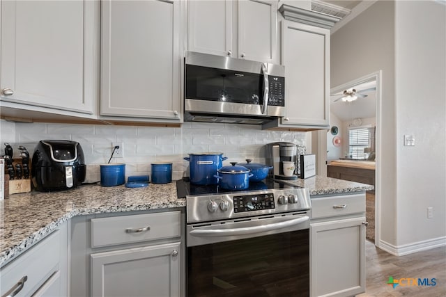 kitchen with stainless steel appliances, white cabinetry, light hardwood / wood-style flooring, and light stone counters