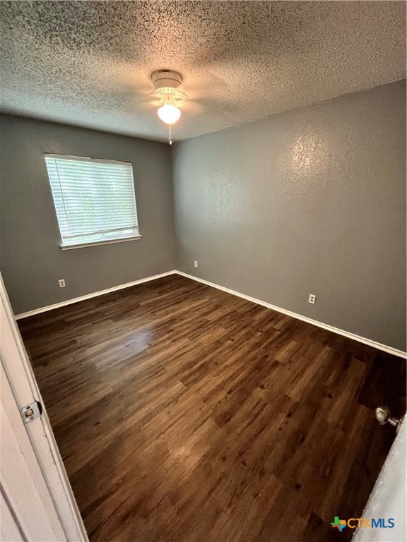 empty room with dark hardwood / wood-style flooring and a textured ceiling