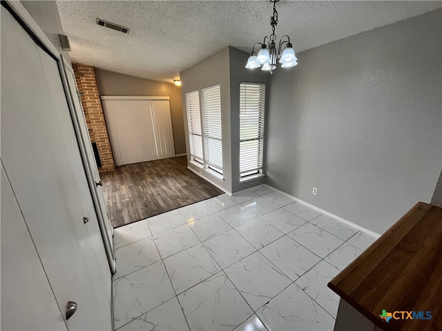 unfurnished dining area with lofted ceiling, light hardwood / wood-style flooring, a chandelier, and a textured ceiling