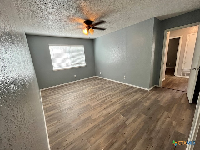 empty room featuring a textured ceiling, ceiling fan, and dark wood-type flooring