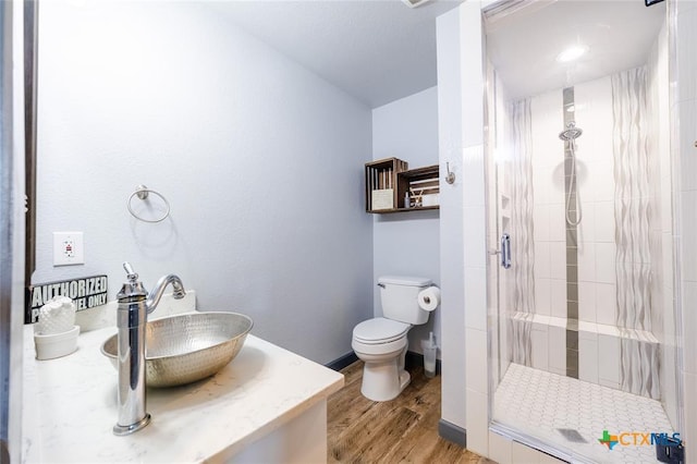 bathroom featuring toilet, wood finished floors, vanity, baseboards, and a stall shower