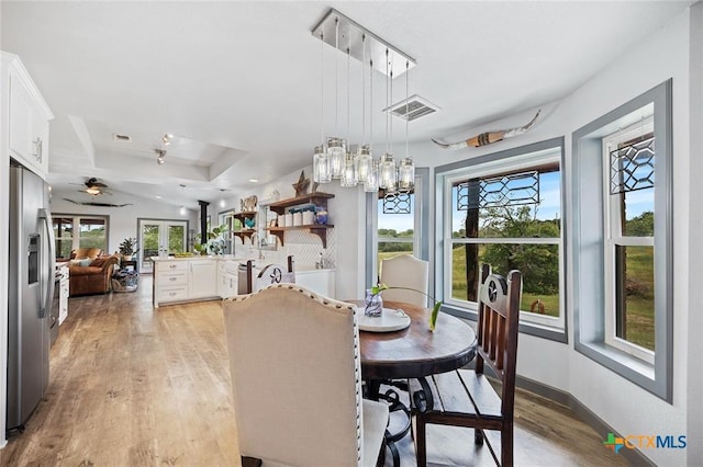 dining space featuring ceiling fan, a tray ceiling, light wood-type flooring, and visible vents