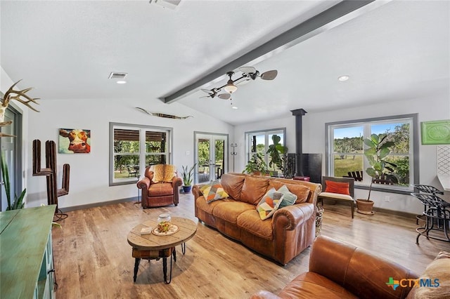 living room featuring lofted ceiling with beams, light wood finished floors, a wood stove, and a healthy amount of sunlight