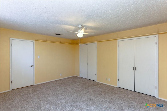 unfurnished bedroom featuring a textured ceiling, light colored carpet, a ceiling fan, multiple closets, and visible vents