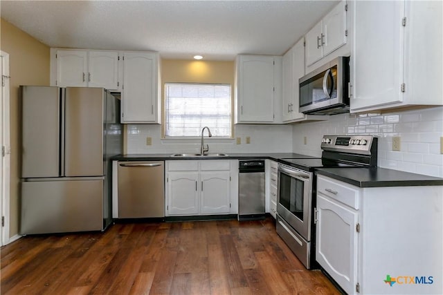 kitchen featuring white cabinets, dark countertops, dark wood-type flooring, stainless steel appliances, and a sink