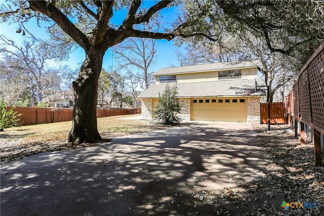 view of front of property with driveway, stone siding, a garage, and fence