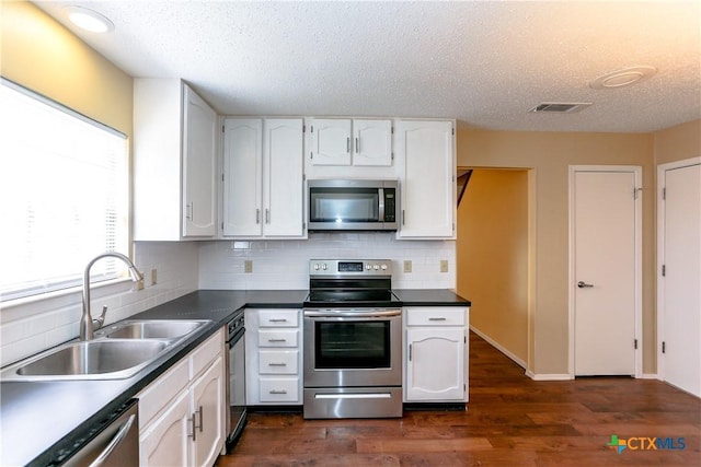 kitchen featuring appliances with stainless steel finishes, dark countertops, a sink, and white cabinets