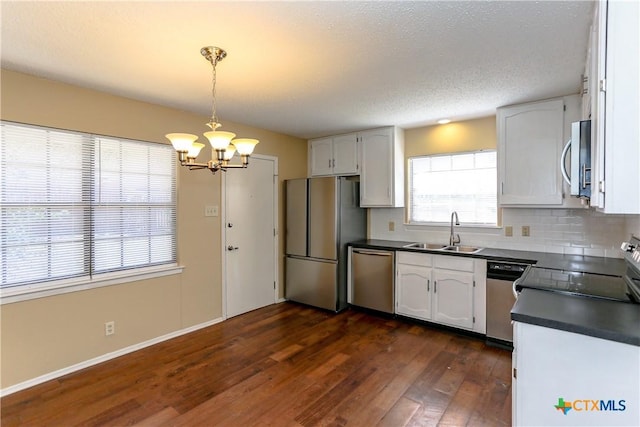 kitchen with decorative light fixtures, stainless steel appliances, dark countertops, white cabinetry, and a sink