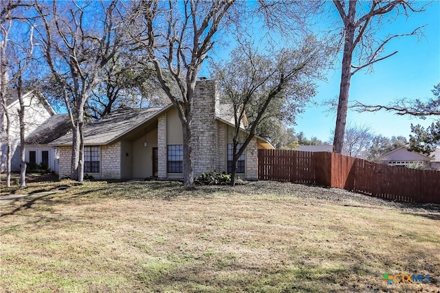 view of side of home featuring stone siding, fence, and a yard