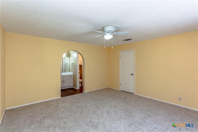 carpeted empty room featuring baseboards, visible vents, arched walkways, a ceiling fan, and a textured ceiling