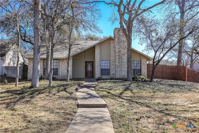 mid-century home with stone siding, a chimney, fence, and a front lawn