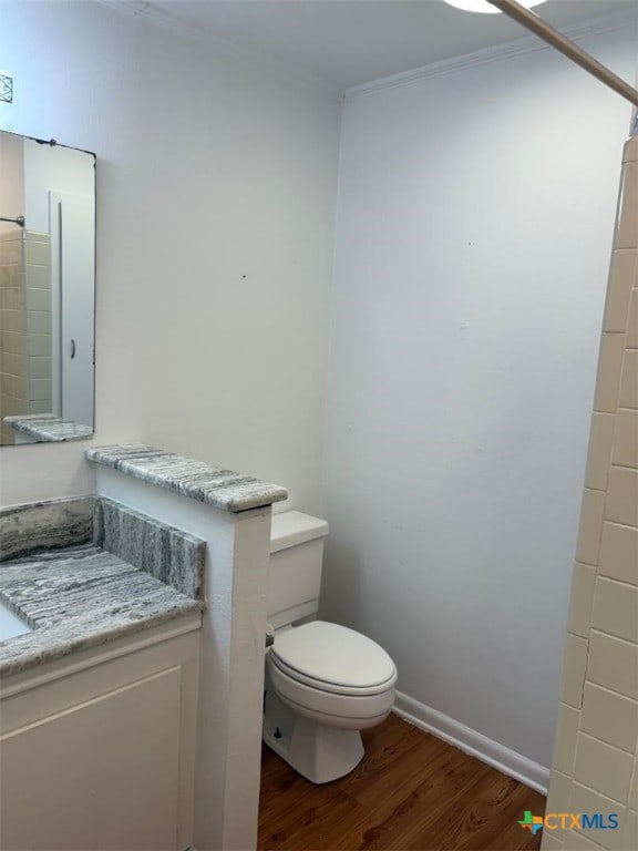 bathroom featuring toilet, wood finished floors, vanity, baseboards, and ornamental molding