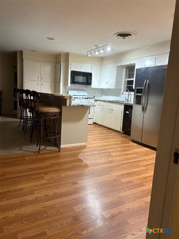 kitchen with light wood-type flooring, white cabinets, visible vents, and black appliances