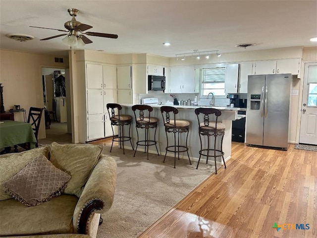 kitchen featuring black microwave, a breakfast bar area, light wood-style flooring, light countertops, and stainless steel fridge