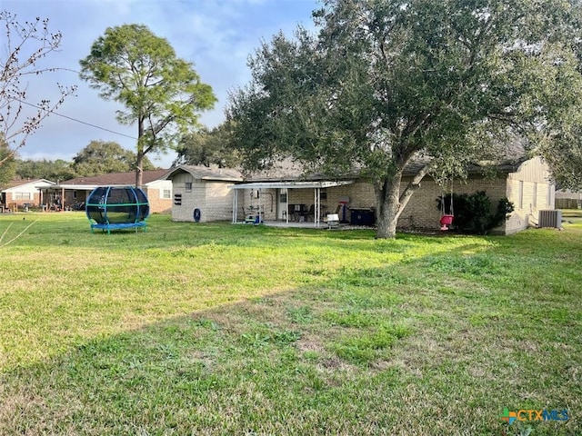 rear view of house with a trampoline, brick siding, a yard, and a patio