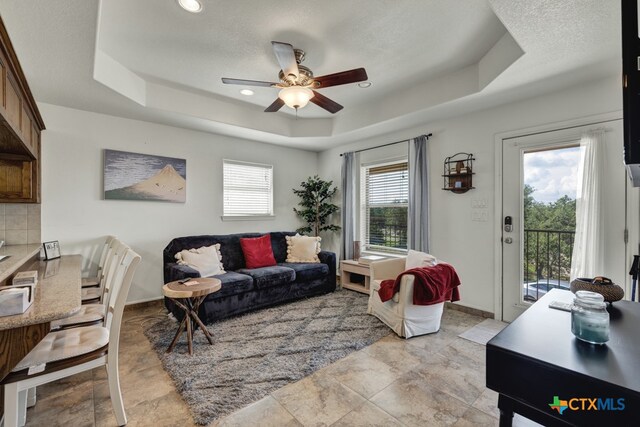 living room with a wealth of natural light, ceiling fan, and a tray ceiling