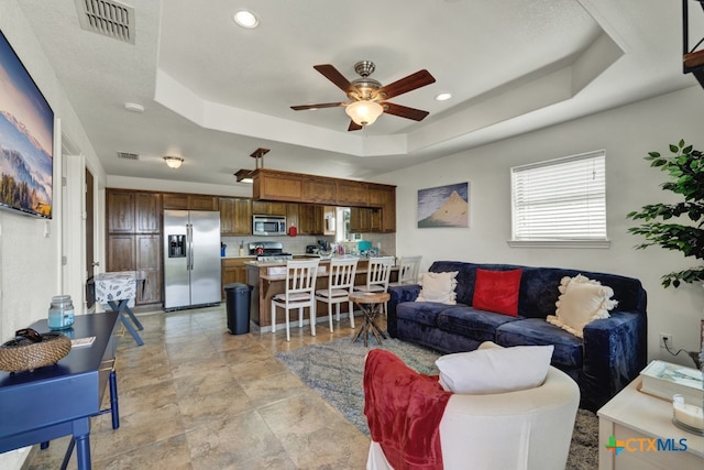 living room featuring ceiling fan and a raised ceiling