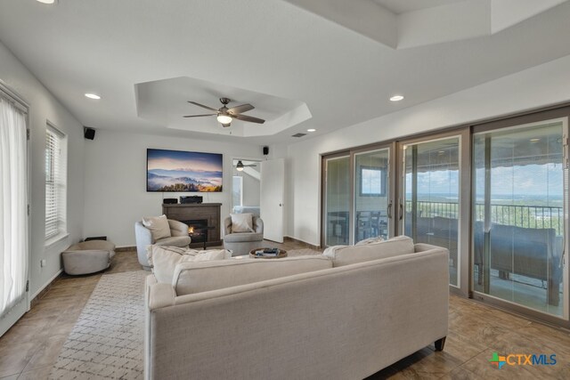 living room with a wealth of natural light, ceiling fan, and a raised ceiling