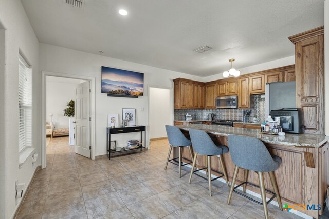 kitchen featuring light stone counters, backsplash, stove, pendant lighting, and a breakfast bar area