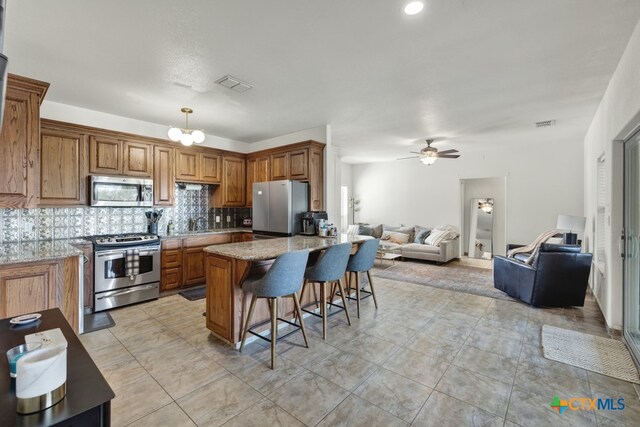 kitchen with stainless steel appliances, a breakfast bar, light stone countertops, ceiling fan with notable chandelier, and decorative backsplash