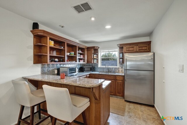 kitchen with appliances with stainless steel finishes, sink, decorative backsplash, a kitchen breakfast bar, and kitchen peninsula