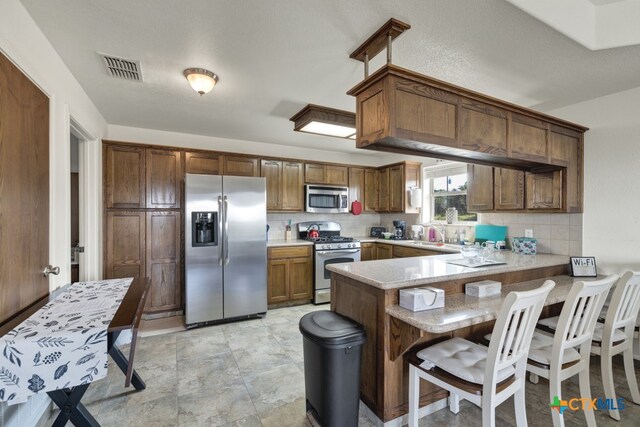 kitchen featuring stainless steel appliances, kitchen peninsula, a breakfast bar area, a textured ceiling, and decorative backsplash