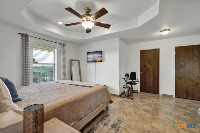 bedroom featuring multiple closets, ceiling fan, and a raised ceiling