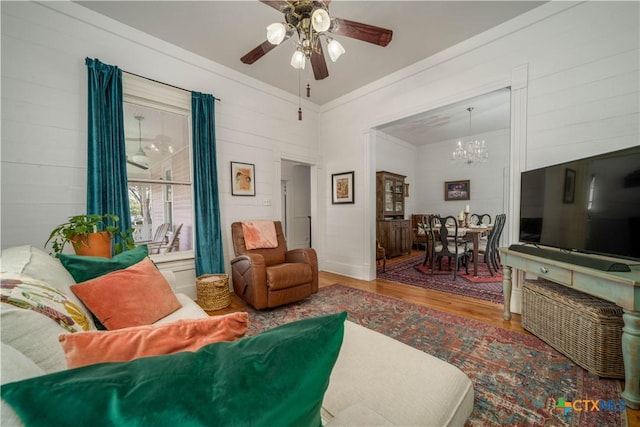 living area featuring ceiling fan with notable chandelier, wood finished floors, and ornamental molding