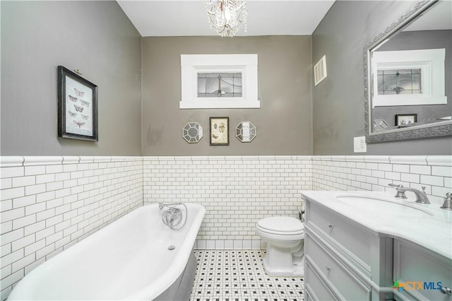 full bathroom with vanity, a wainscoted wall, an inviting chandelier, a freestanding tub, and toilet