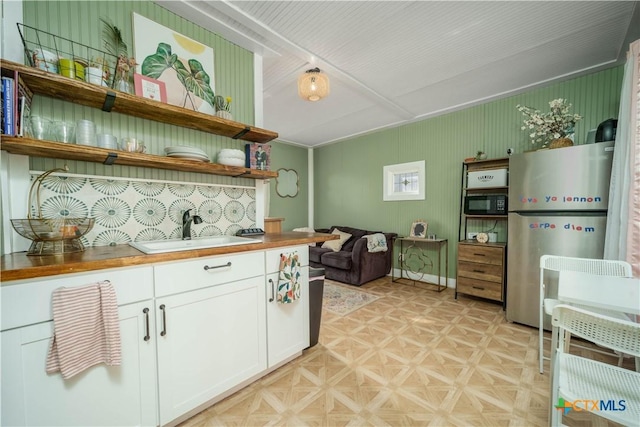 kitchen with a sink, black microwave, freestanding refrigerator, white cabinetry, and open shelves