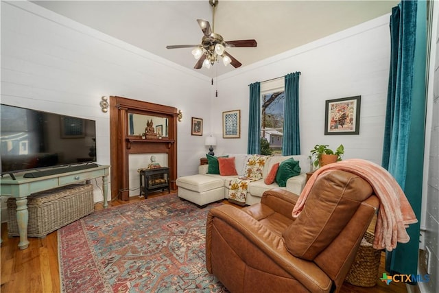 living room featuring a ceiling fan, crown molding, a wood stove, and wood finished floors