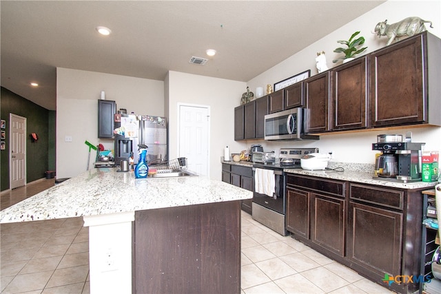 kitchen with light tile patterned flooring, appliances with stainless steel finishes, dark brown cabinetry, and a center island with sink