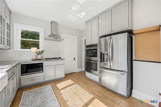610 N 7th St, Temple, TX 76501 - kitchen featuring appliances with stainless steel finishes, wall chimney range hood, decorative backsplash, light wood-style floors, and light stone countertops