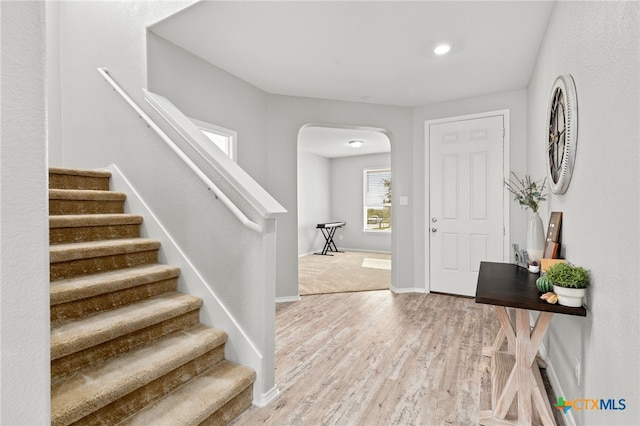 foyer entrance featuring arched walkways, stairway, light wood-type flooring, and baseboards