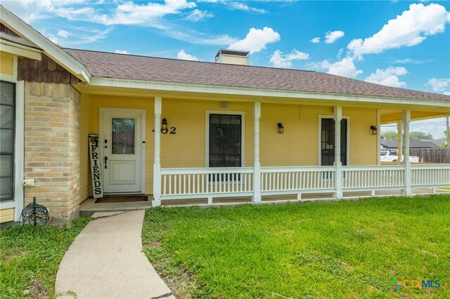 402 Teakwood Dr, Victoria, TX 77901 - doorway to property featuring covered porch, a yard, roof with shingles, and a chimney