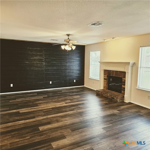 unfurnished living room featuring dark wood-type flooring, ceiling fan, a textured ceiling, and a brick fireplace