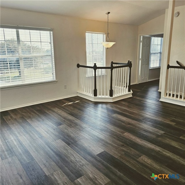 unfurnished room with a wealth of natural light, vaulted ceiling, and dark hardwood / wood-style floors