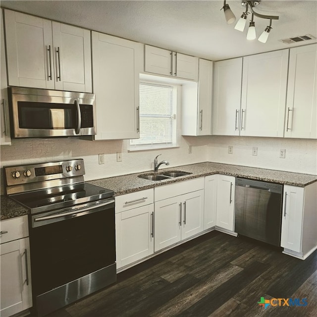 kitchen with dark stone counters, white cabinetry, appliances with stainless steel finishes, sink, and dark wood-type flooring