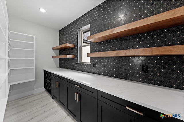kitchen featuring open shelves, light wood-style floors, dark cabinetry, wallpapered walls, and decorative backsplash