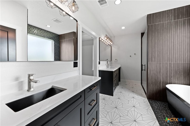 bathroom featuring visible vents, tile patterned flooring, two vanities, a soaking tub, and a sink