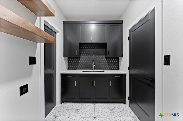 kitchen featuring a sink, light countertops, dark cabinets, decorative backsplash, and light tile patterned floors