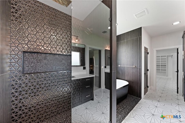 full bathroom with a walk in closet, vanity, tile patterned floors, recessed lighting, and a soaking tub