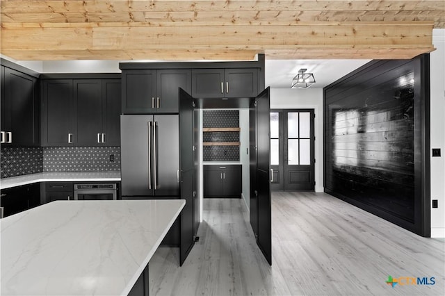 kitchen with light stone countertops, tasteful backsplash, dark cabinetry, light wood-style flooring, and appliances with stainless steel finishes