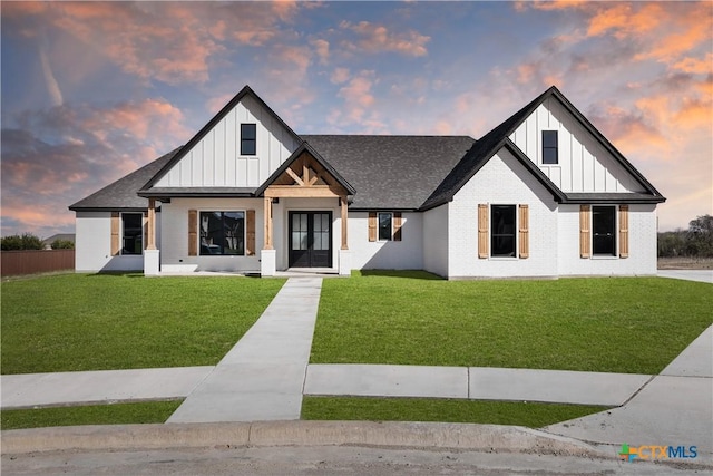 modern inspired farmhouse featuring brick siding, a shingled roof, board and batten siding, and a front yard