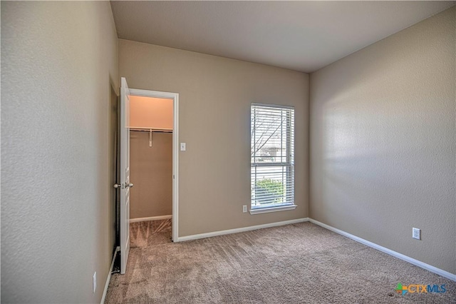 unfurnished bedroom with a textured wall, carpet flooring, a walk in closet, and baseboards