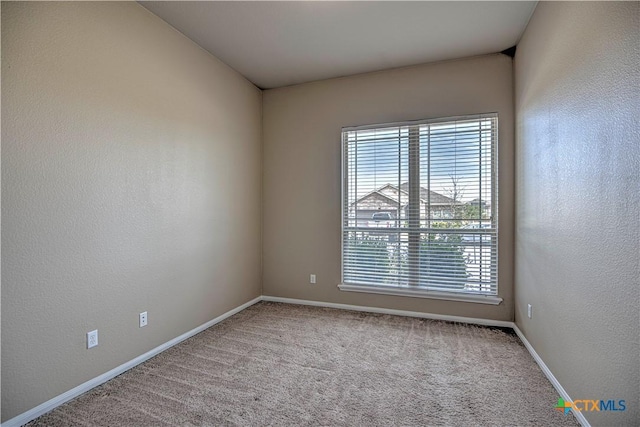 carpeted spare room featuring a textured wall and baseboards