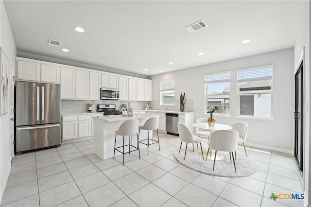 kitchen with appliances with stainless steel finishes, tasteful backsplash, white cabinets, a kitchen island, and light countertops